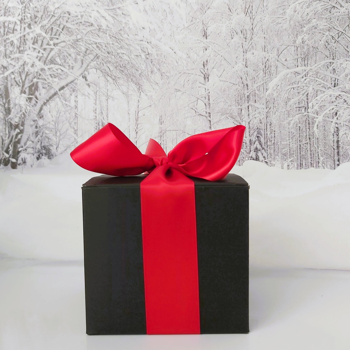 Black gift box with a red ribbon against a snowy forest background