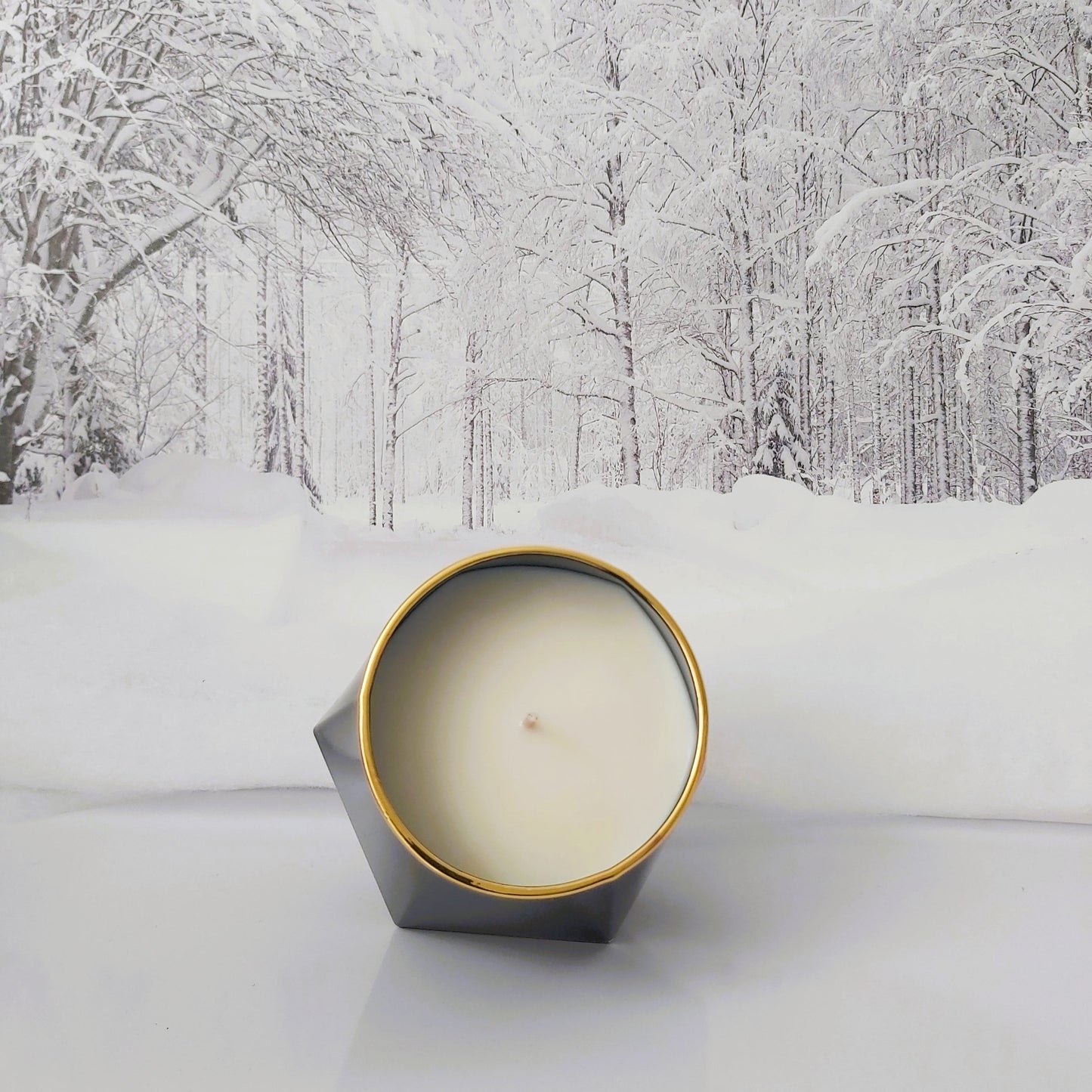 Candle in a geometric tin with a snowy forest background