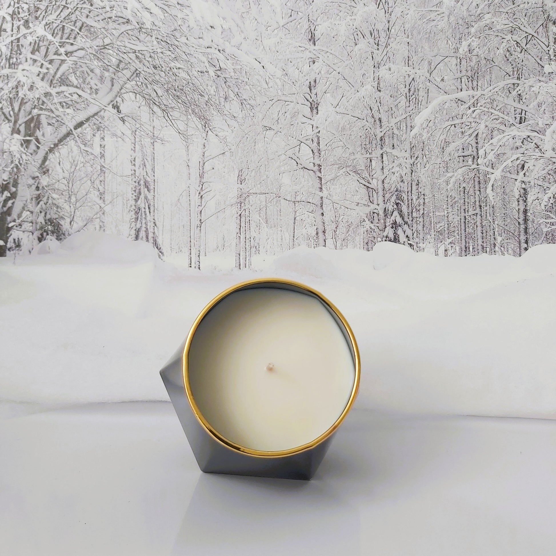 Candle in a geometric tin with a snowy forest background
