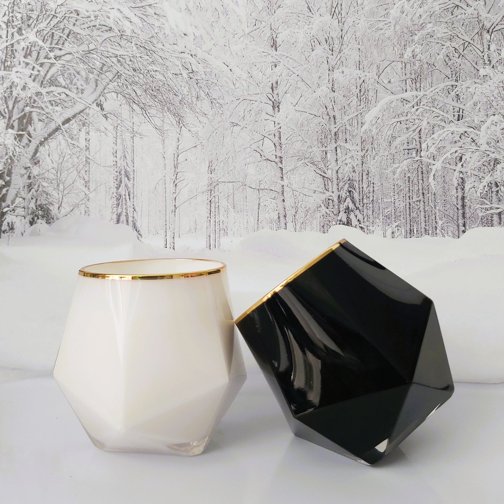 Two geometrically shaped candles, one white and one black, against a snowy forest background.