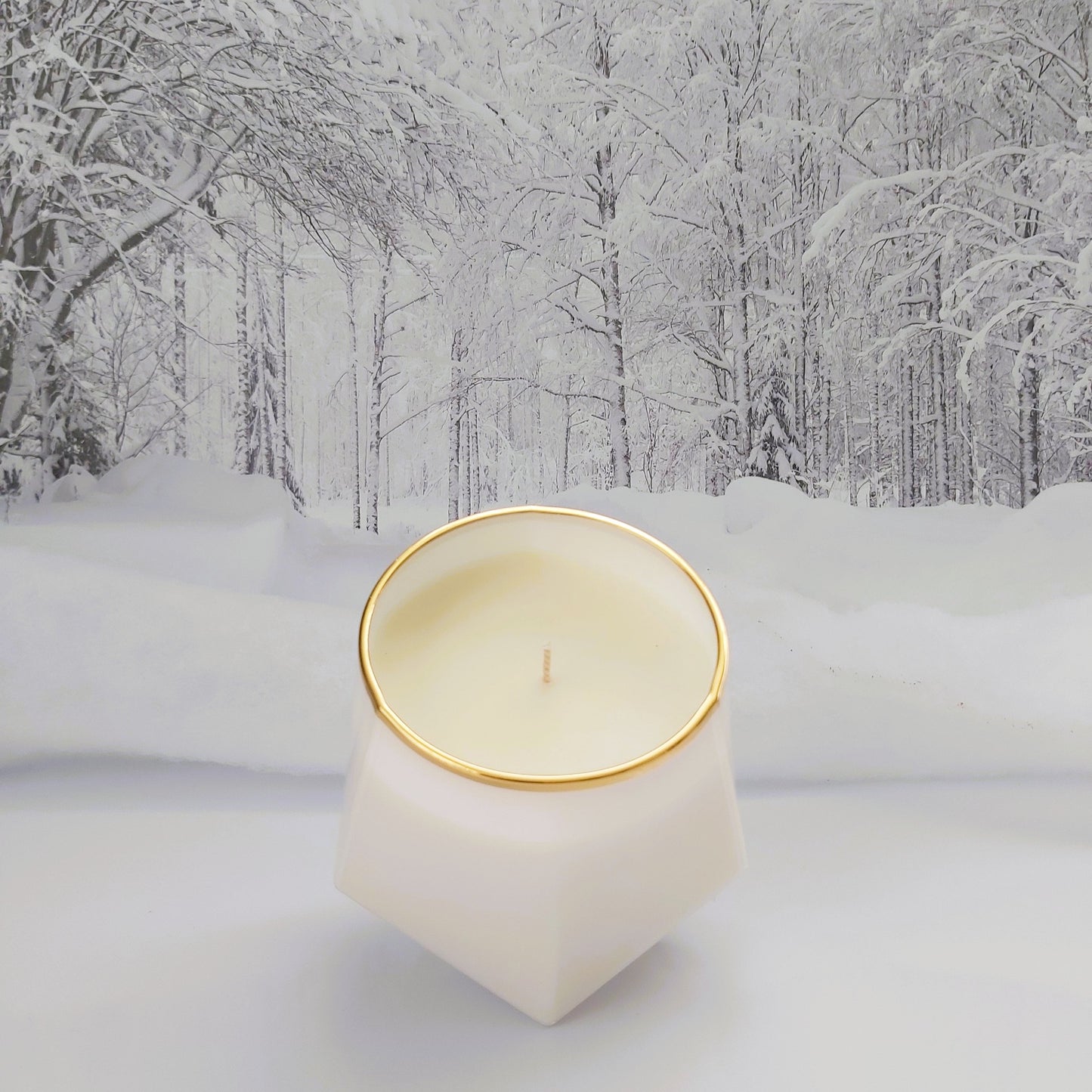 Candle in a geometric holder with gold rim on a snowy landscape