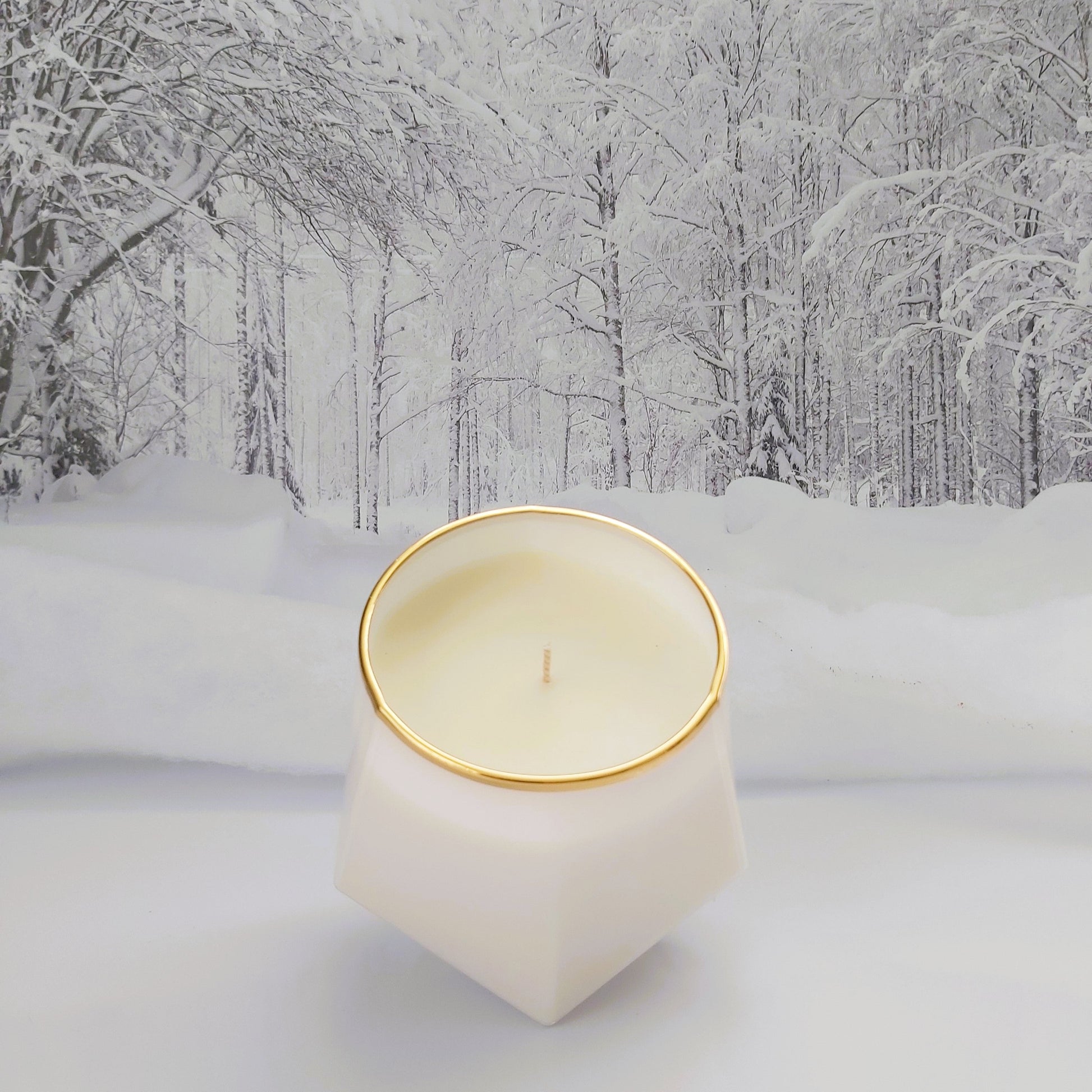Candle in a geometric holder with gold rim on a snowy landscape