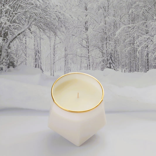 Candle in a geometric holder with gold rim on a snowy landscape