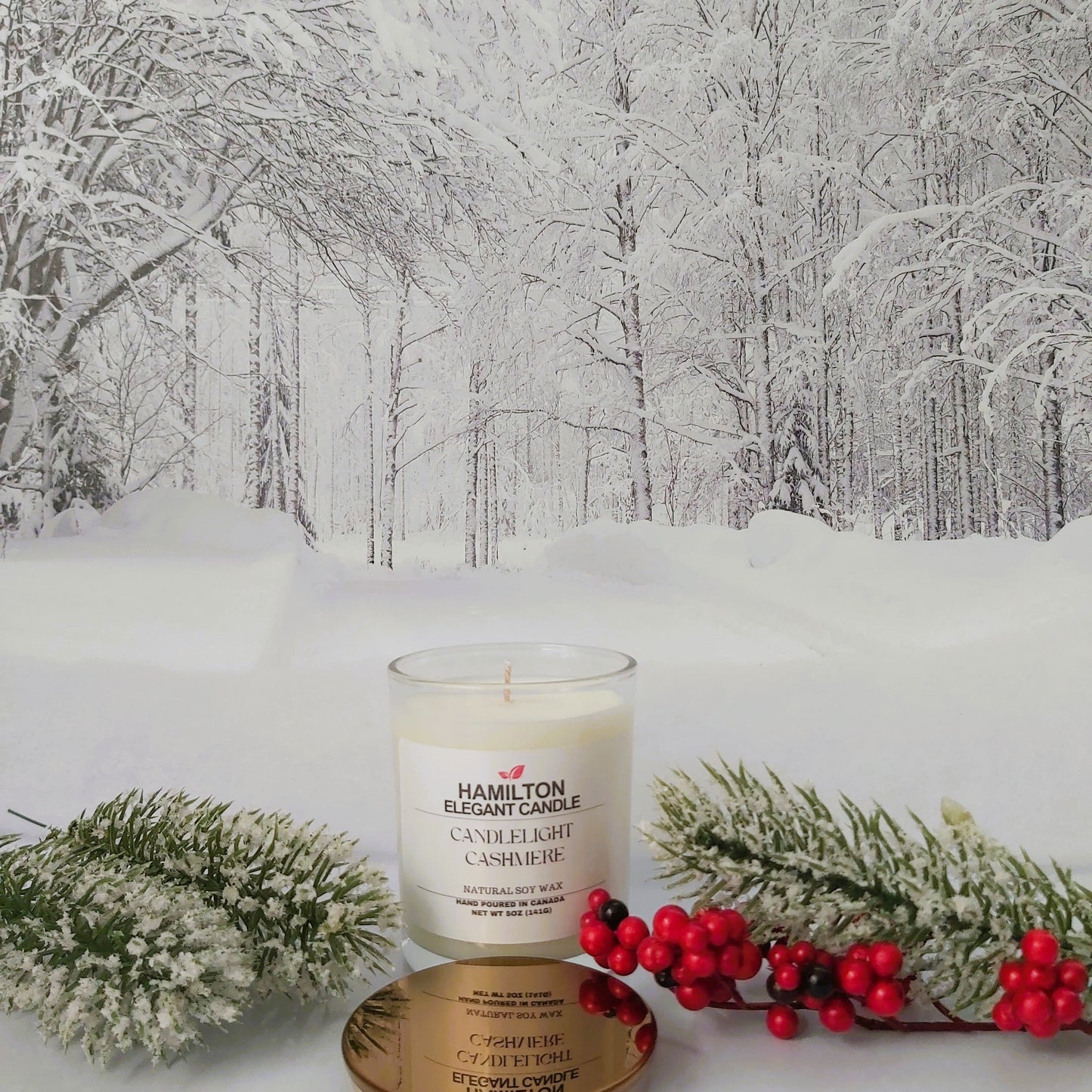 Candle with wintery scene of snow-covered trees and berries